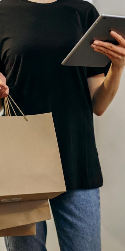 Woman in black shirt with shopping bags using a tablet at home, symbolizing online shopping convenience.